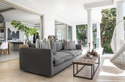Grey sofa, coffee table and hanging chair on roofed terrace