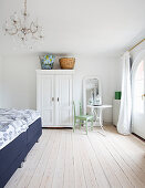White wardrobe, round table and chair and double bed in bedroom with pale wooden floor