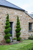 In Spiralform geschnittene Hecken am Eingang eines Natursteinhauses