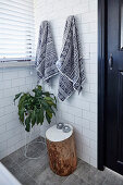 Towels, houseplant and tree stool in the bathroom with white wall tiles