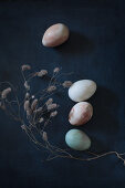 Dried flowers around painted eggs on black surface