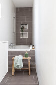 Bathtub in narrow bathroom with light grey tiles on floor and back wall