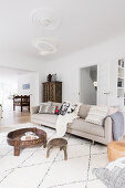 Pale sofa with scatter cushions, coffee table and antique wooden cupboard in open-plan interior