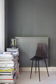 Black chair and stacked magazines in front of radiator on dark wall