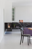 Chair in front of L-shaped, floating, black marble shelf with integrated fireplace