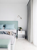 Custom-made double bed with mint green headboard, bedside table and wall lamp in the bedroom
