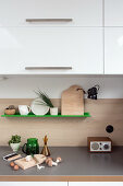 Chopping board on grey worksurface below green shelf and wall units in kitchen