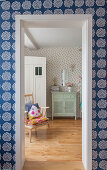 View through open door in wall with polka-dot wallpaper into bedroom