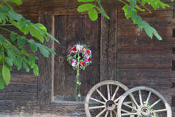 Door wreath of sage leaves, dahlias, phlox and green physalis husks next to old wooden wheels