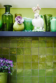 Dekovogel und grüne Vasen auf dem Regal an grüner Wand
