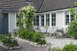 Hof mit Blumenbeeten und Terrasse vorm weißen Schwedenhaus