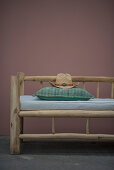 Cowboyhut und Kissen auf rustikaler Holzbank vor rosafarbener Wand