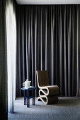 Designer chair and side table with teapot in front of a dark curtain