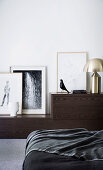 Sideboard mit Kunstwerken und Bett mit schwarzer Decke im Schlafzimmer