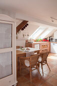 Massivholztisch mit Rattansesseln unter Dachschräge in offener Küche
