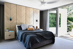 Doppelbett am Raumteiler aus Holzfurnier im Schlafzimmer mit Terrasssenzugang