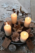 Lit candles on plate with fabric flowers and paper snowflakes