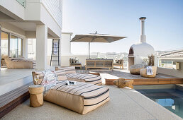 Floor cushions next to pool on roof terrace with lounge area and wood-fired oven