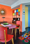 Essbereich vor Sideboard in Retro Ambiente mit orangefarbener Wand
