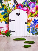 Small wooden door in front of non-woven wallpaper with flower meadow in the children's room