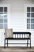 Black wooden bench with scatter cushion outside wooden house