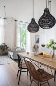 Dining table and various chairs below black pendant lamps in open-plan interior
