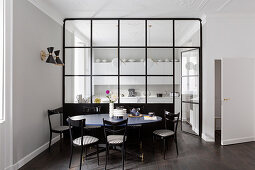 Black chairs around dining table in front of glass partition wall looking into kitchen