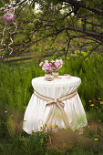 Ornate tablecloth and peonies on round table below tree