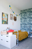 Grey metal bed against blue-patterned retro wallpaper in child's bedroom