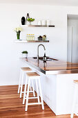 Two stools at white island counter with wooden worksurface and sink