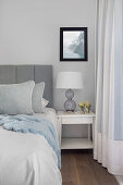 Bed with grey headboard and white bedside table in bedroom