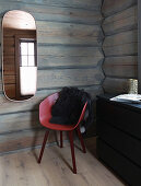 Oval mirror above red shell chair in log cabin