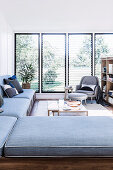 L-förmige Couch, Couchtisch und Sessel vor Fenster in hellem Wohnbereich