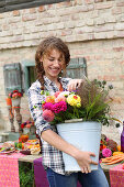 Smiling woman carrying a bucket of brightly coloured autumn flowers