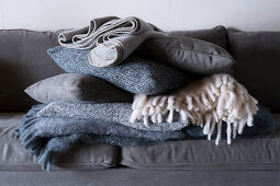 Stack of folded woollen blankets and cushions on grey sofa