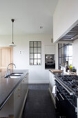 Küchenzeile mit Gasherd und Mittelblock in Küche mit weißen Wänden und schwarzen Fliesenboden