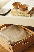 Blanket in wooden box under books and bowls on coffee table