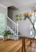 Vase of flowers on glass table and foot of staircase in foyer with whitewashed brick wall