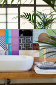 Folded towels next to countertop sink on washstand with multicoloured tiled splashback in bathroom