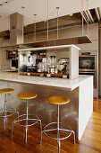 Various kitchen devices on island counter and barstools in elegant, open-plan kitchen
