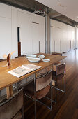 Long wooden table and chairs with suede covers in front of fitted cupboards in loft apartment