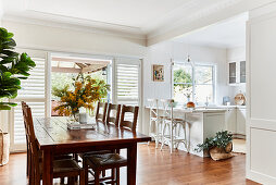 Rustic wooden table and chairs in dining area; white kitchen counter with barstools in background