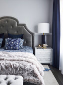 Double bed with bed headboard on light gray wall and elegant bedside table with table lamp