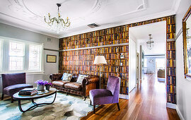 Leather sofa and floor lamp in front of vintage library wallpaper, purple upholstered chairs and coffee table in living room