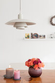 Vase of roses and two candles on wooden table below classic pendant lamp