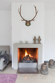 Fire in fireplace below antlers on wall