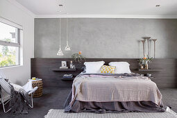 Wandpaneel aus dunklem Holz hinter dem Bett an grauer Wand
