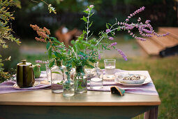 Flowers in apothecary bottles on set table in garden