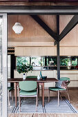 Open kitchen with light wooden front and mirrored back wall, in the foreground dining table with green upholstered chairs