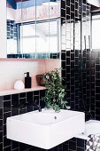 Weißes Wascchbecken und Spiegelschrank im Badezimmer mit schwarzen Wandfliesen